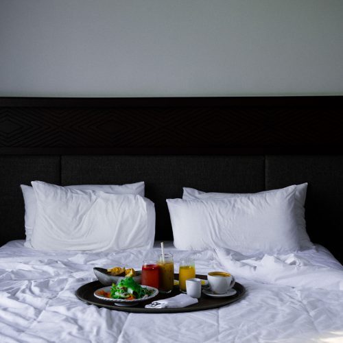 Petit-déjeuner servi sur un lit d’hôtel à Amber Kampot, avec jus frais, café et plats disposés sur un plateau.