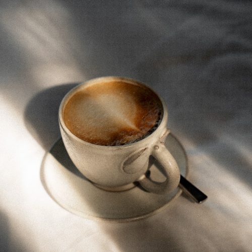 Tasse de café posée sur une table, éclairée par une lumière naturelle douce à l’hôtel Amber Kampot.