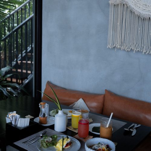 Petit-déjeuner servi à table avec plats et jus frais dans l’ambiance végétale de l’hôtel Amber Kampot.