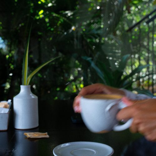 Main servant une boisson chaude sur une table, dans une ambiance végétale à l’hôtel Amber Kampot.