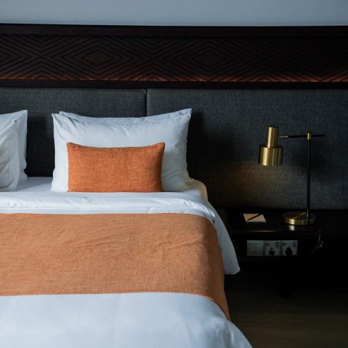 Lit d’hôtel avec linge blanc et jeté terracotta dans une chambre design de l’hôtel Amber Kampot.