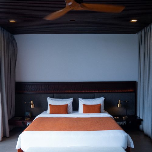 Chambre design de l’hôtel Amber Kampot avec lit double, linge blanc et ventilateur de plafond en bois.