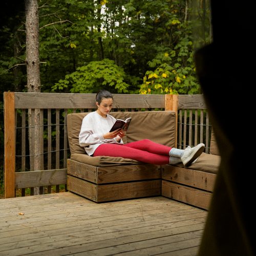 Personne lisant sur une terrasse en bois au cœur de la forêt chez Huttopia à Sutton, Québec