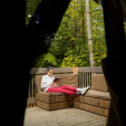 Personne lisant sur une terrasse en bois entourée par la forêt chez Huttopia à Sutton, Québec