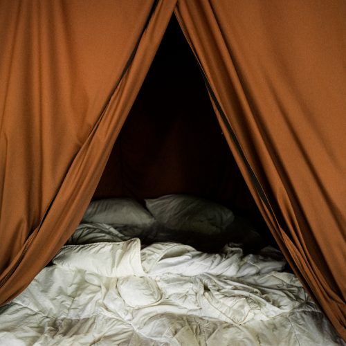 Lit double à l’intérieur d’une tente Huttopia, draps blancs et toile beige, ambiance cosy en pleine nature à Sutton