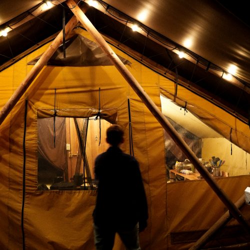 Personne entrant dans une tente Huttopia éclairée de nuit, ambiance glamping en pleine nature à Sutton