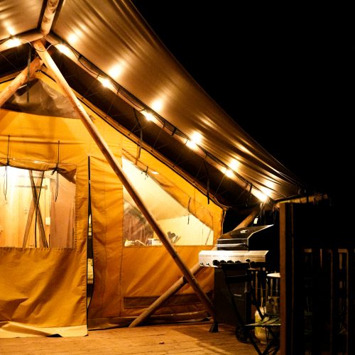 Tente Huttopia éclairée de nuit avec terrasse en bois et barbecue, expérience glamping à Sutton