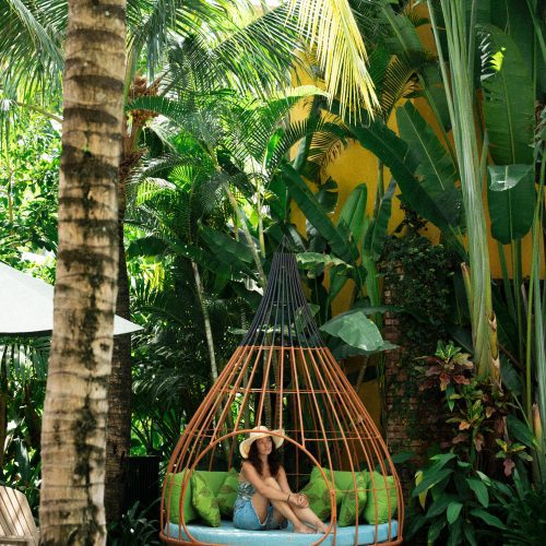 Personne assise dans un fauteuil suspendu près de la piscine, entourée de végétation tropicale à La Siesta Hoi An.