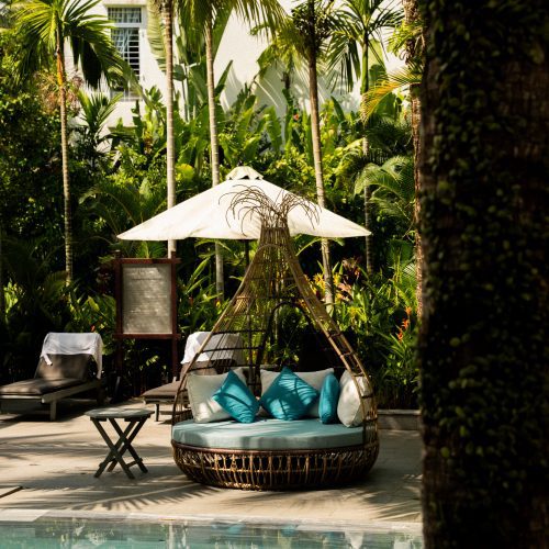 Espace détente au bord de la piscine de La Siesta Hoi An, entouré de palmiers et de végétation tropicale.