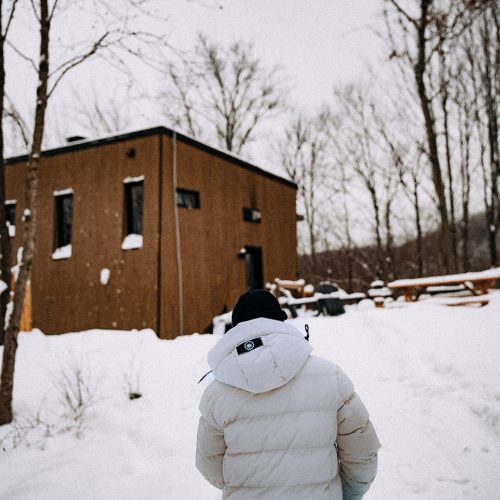 Personne marchant dans la neige avec une luge près d’un chalet du domaine Le Vertendre en hiver.