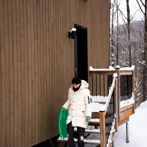 Personne descendant les marches d’un chalet du domaine Le Vertendre en hiver avec une luge.
