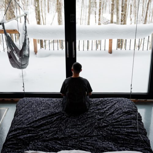Personne assise face à une grande baie vitrée donnant sur la forêt enneigée au Vert Tendre