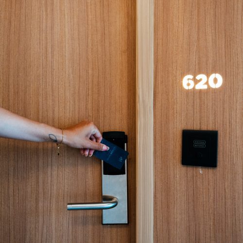 Une main présente une carte de chambre devant la serrure d’une porte en bois marquée 620 au Maison Hotel Bangkok.