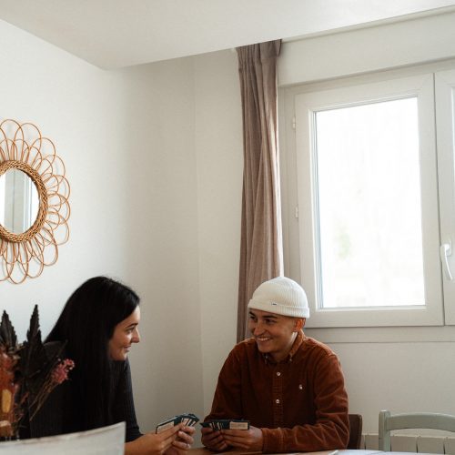 Deux personnes assises à une table dans un gîte du Mas Cantegril, échangeant dans une ambiance conviviale et lumineuse.