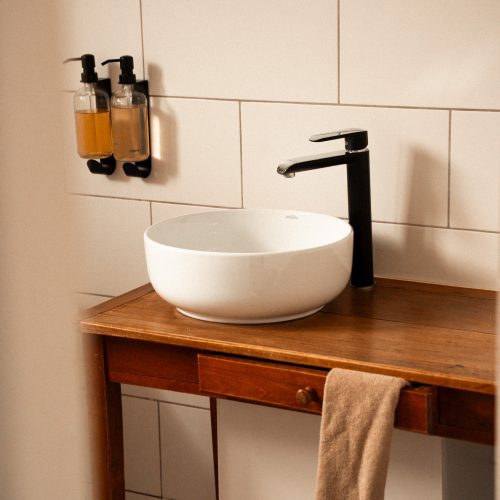 Lavabo et robinetterie dans la salle de bain d’un gîte du Mas Cantegril, avec meuble en bois et accessoires muraux.