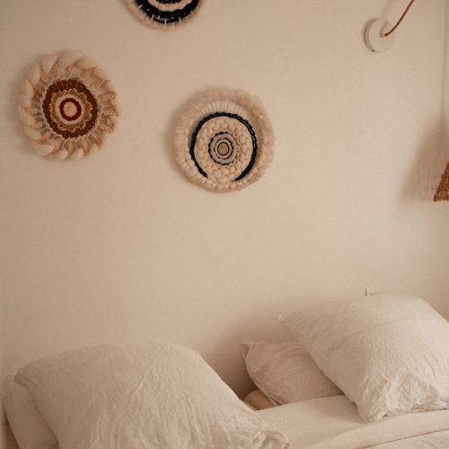 Lit dans une chambre d’un gîte du Mas Cantegril, avec oreillers clairs et décoration murale textile.