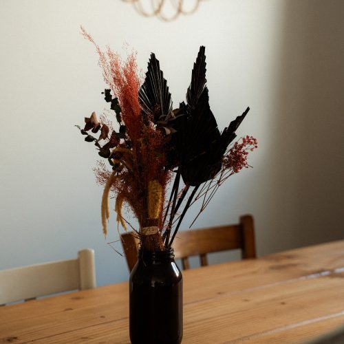 Vase avec fleurs séchées posé sur une table en bois dans un gîte du Mas Cantegril.