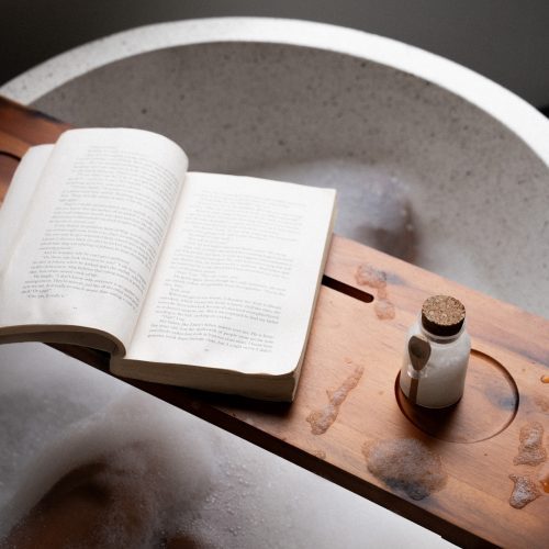 Plateau en bois avec un livre et un flacon posé sur une baignoire dans la suite du Meander Saigon.