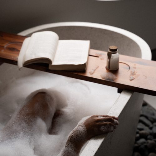 Main reposant sur le rebord d’une baignoire remplie de mousse dans la suite de l’hôtel Meander Saigon.