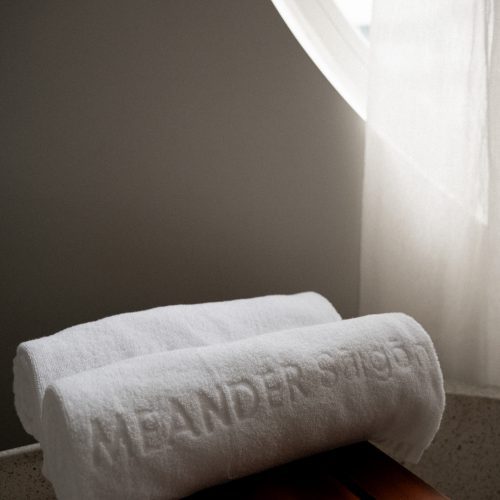 Serviettes blanches roulées posées sur un plateau en bois dans la salle de bain de la suite du Meander Saigon.