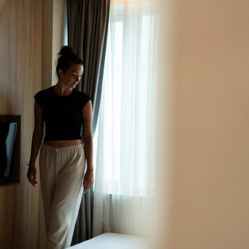 Personne debout près du lit dans la chambre Double Supérieure de l’hôtel Meander Saigon, éclairée par une fenêtre.