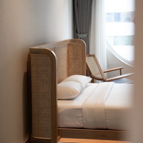 Lit et fauteuil près d’une fenêtre circulaire dans la chambre Double Deluxe de l’hôtel Meander Saigon.