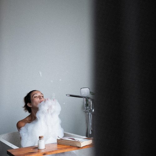 Personne prenant un bain dans une baignoire de l’hôtel Meander Saigon, avec un plateau posé sur le rebord.