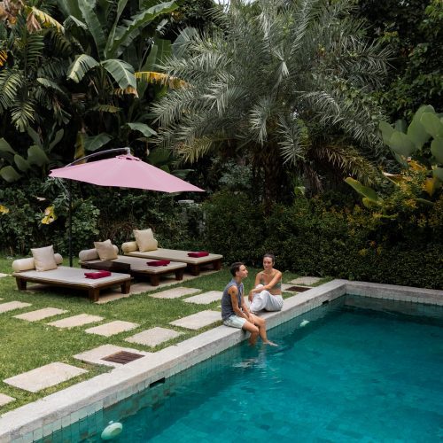 Un couple assis au bord d’une piscine entourée d’un jardin tropical au Parasol Blanc à Luang Prabang.