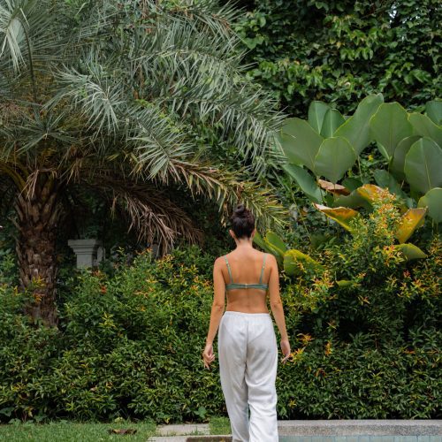 Femme marchant pieds nus au bord de la piscine dans le jardin du Parasol Blanc à Luang Prabang.