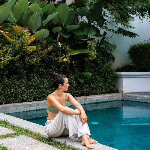 Femme assise au bord de la piscine du Parasol Blanc, entourée de végétation tropicale à Luang Prabang.