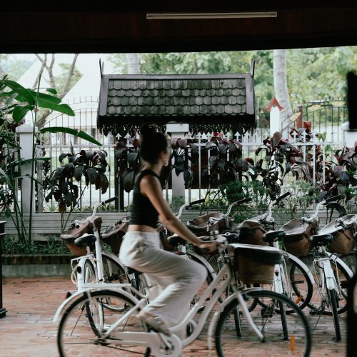 Personne circulant à vélo dans la cour du Parasol Blanc à Luang Prabang, avec plusieurs vélos stationnés en arrière-plan.