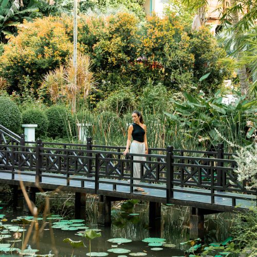 Femme debout sur un pont en bois au-dessus d’un bassin avec nénuphars au Parasol Blanc à Luang Prabang.