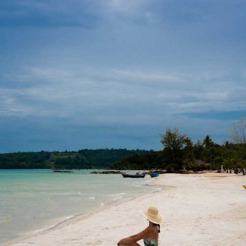 Femme assise sur la plage de sable blanc au The Secret Garden Koh Rong, hôtel en bord de mer au Cambodge, photo par Chloé et Aurore.