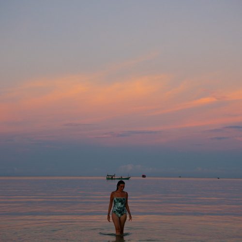 Femme marchant dans la mer au coucher du soleil au The Secret Garden Koh Rong, Cambodge, photo ChloéandAurore.