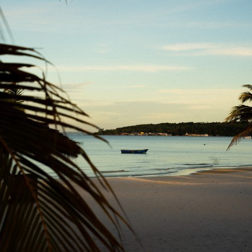 Plage de sable blanc au The Secret Garden Koh Rong avec bateau sur la mer calme au Cambodge, photo chloeandaurore.