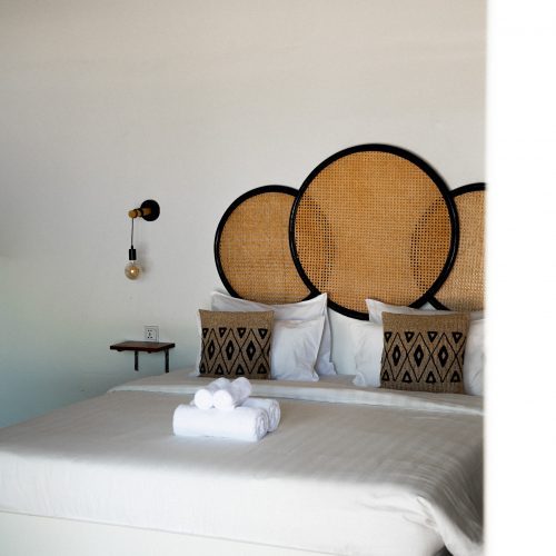 Chambre lit king-size supérieure au Secret Garden Koh Rong avec tête de lit en rotin et linge blanc.