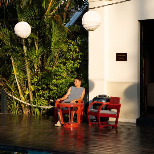 Personne assise au bord de la piscine du Villa Maly à Luang Prabang, entourée de végétation tropicale et d’architecture coloniale.