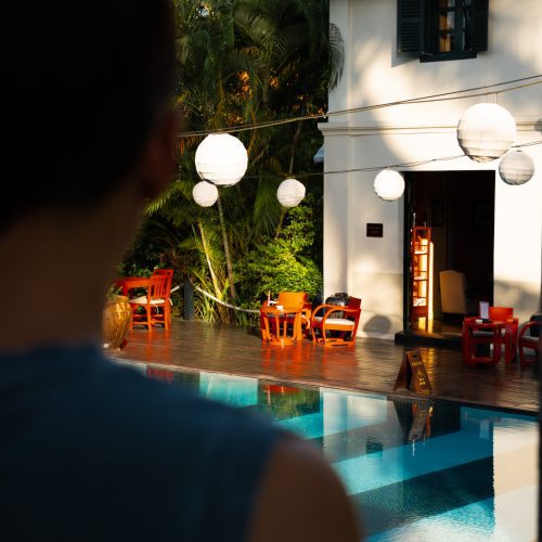Vue sur la piscine et la terrasse en bois du Villa Maly à Luang Prabang, entourées d’un jardin tropical luxuriant, photographiées par chloeandaurore.