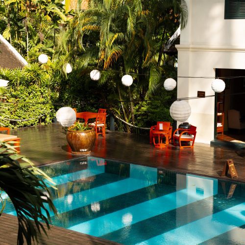 Piscine du Villa Maly à Luang Prabang entourée de végétation tropicale, terrasse en bois et lanternes blanches suspendues.