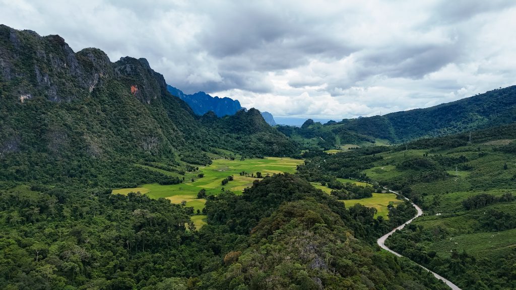 Vallée verdoyante avec rizières et route sinueuse au cœur des montagnes karstiques, paysage rural du Laos